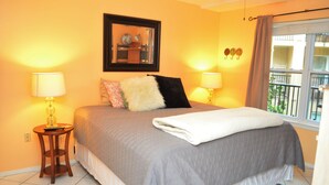 A bedroom with a bed, two bedside lamps, a ceiling fan, a window with curtains, and a framed picture on the wall. - Island Oasis Surfside 208 (South Padre Island)