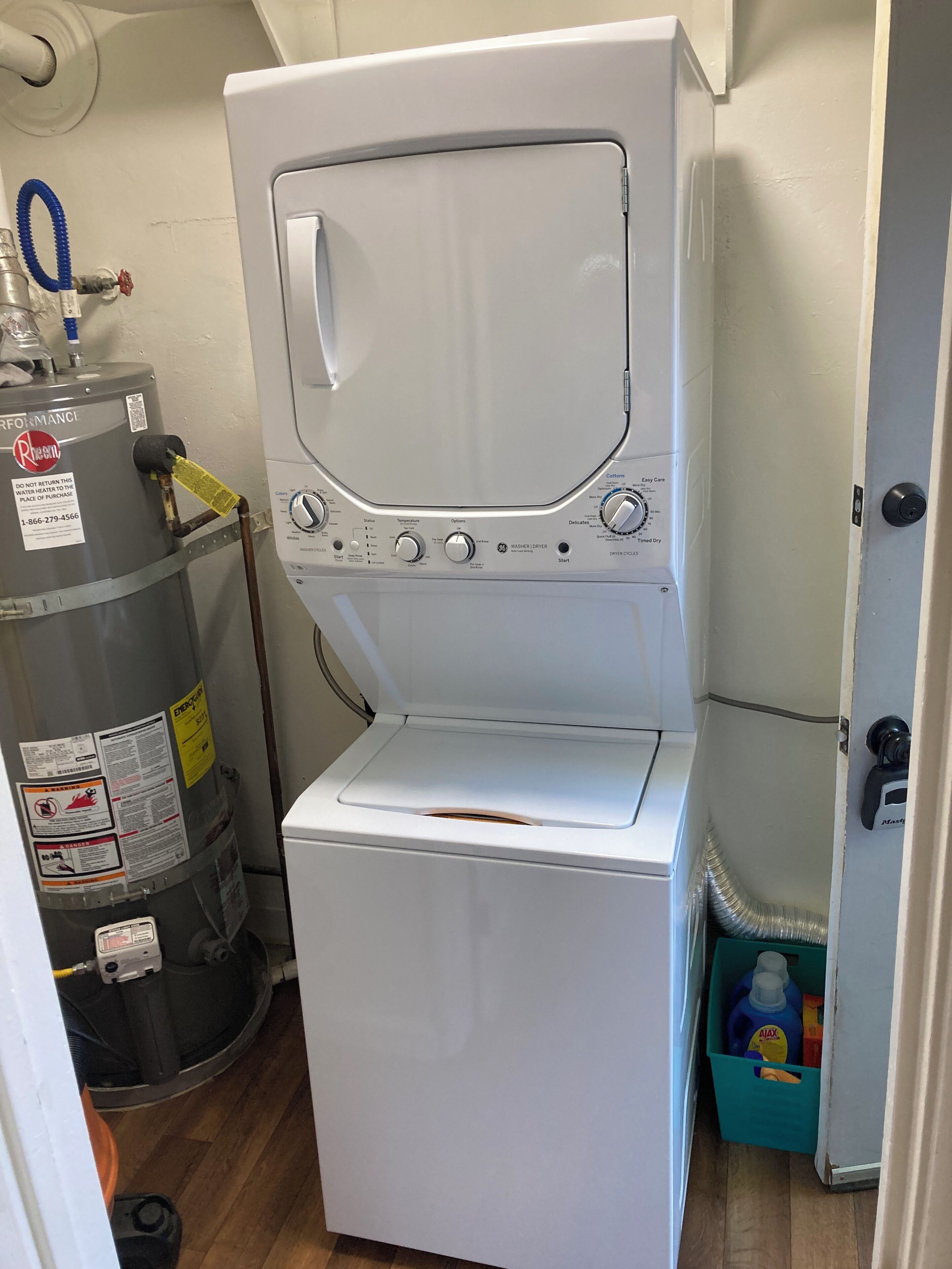 A compact washer and dryer unit with a control panel, a water heater, and a blue storage bin with cleaning supplies.