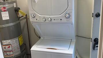 A compact washer and dryer unit with a control panel, a water heater, and a blue storage bin with cleaning supplies.