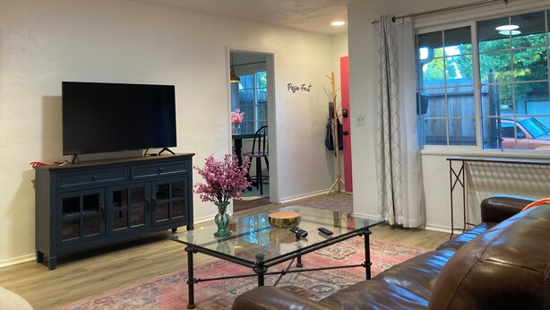 A living room with a TV, dark wooden cabinet, glass coffee table, and a leather sofa. - Charming Bright Home Near Dr Hospital & Shopping - Extra Comfy Beds and Couch (Modesto)