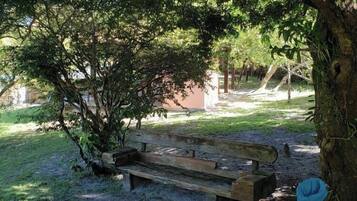 A park with a wooden bench under a tree, surrounded by grass and a playground.