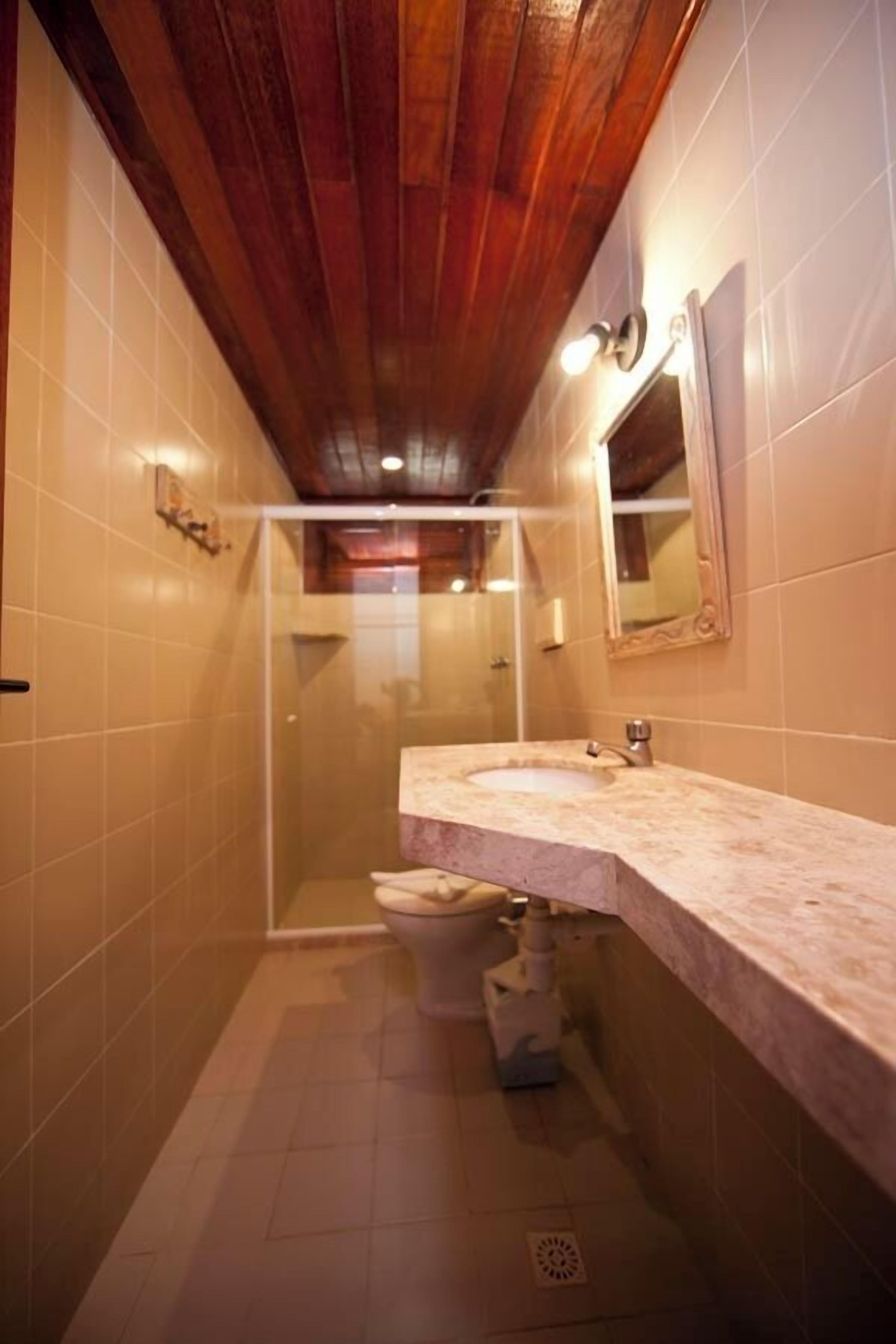 A bathroom with a wooden ceiling, a glass shower enclosure, and a marble sink.