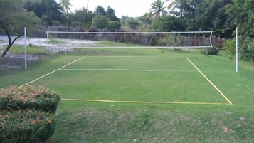 Una cancha de tenis bien cuidada con una red en el centro, rodeada de abundante follaje y árboles.