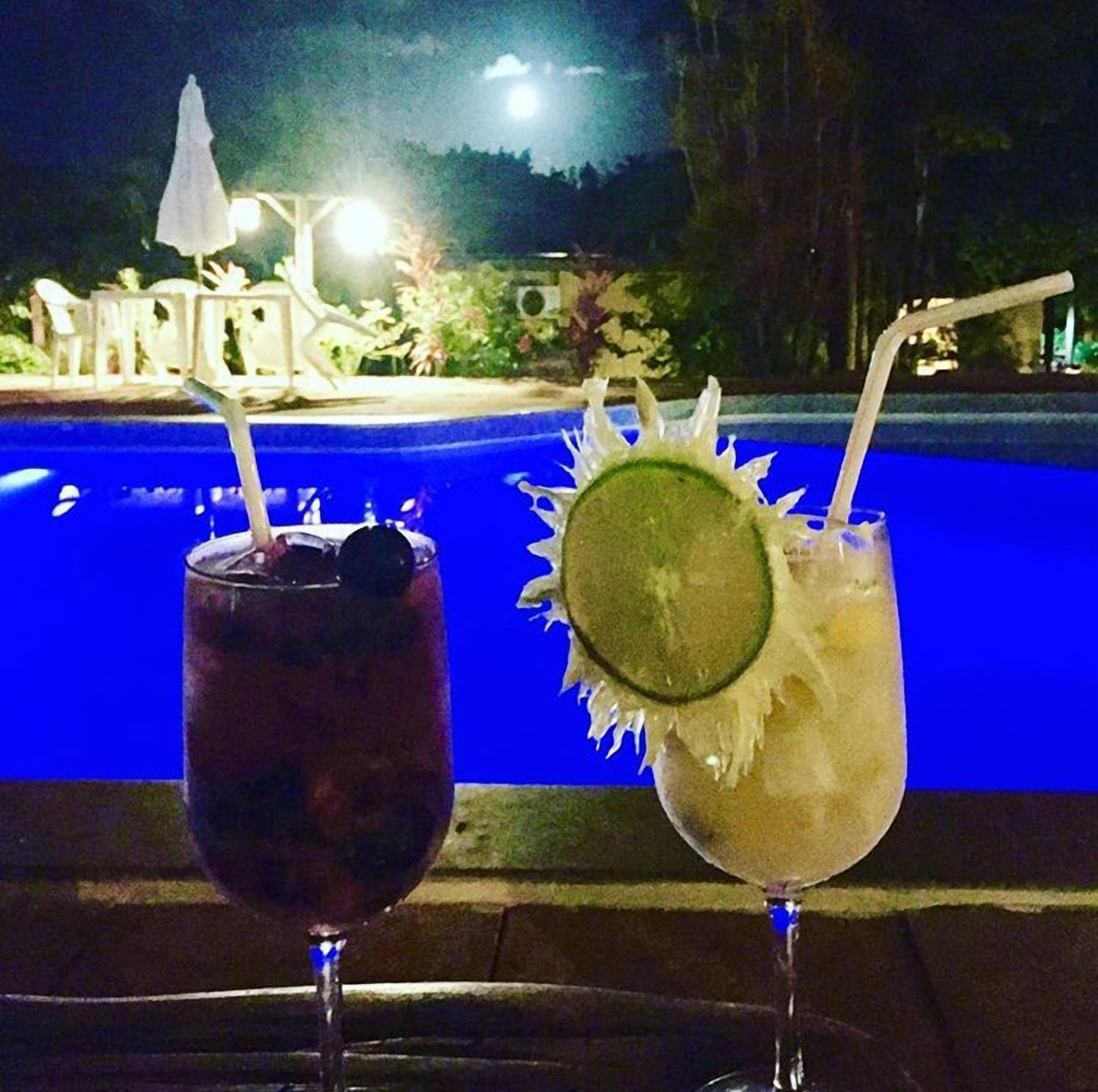 Two drinks with straws and garnishes in front of a pool.