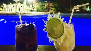 Two drinks with straws and garnishes in front of a pool.