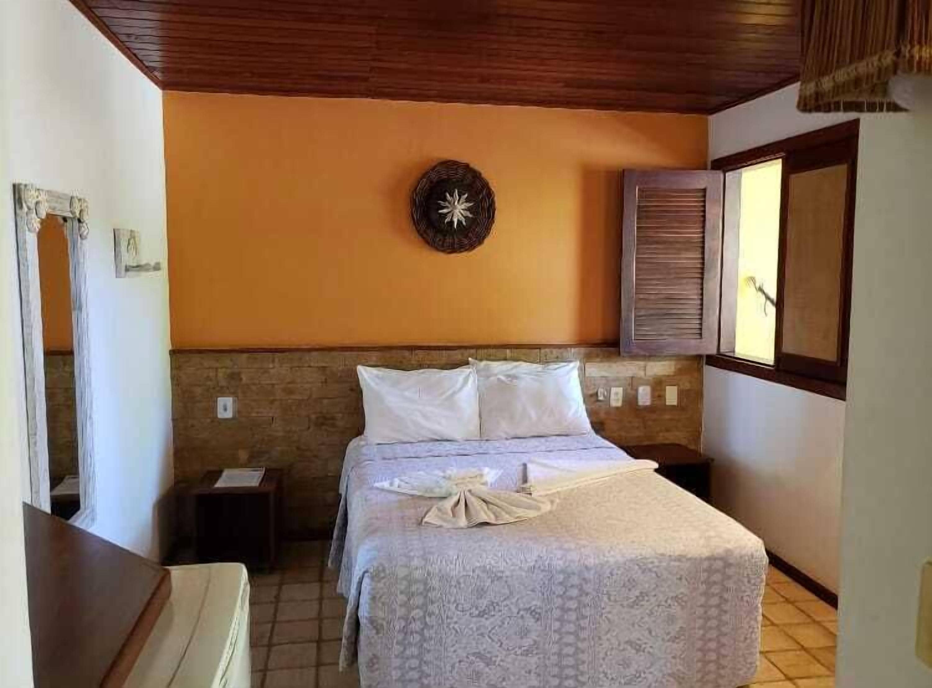 Un dormitorio con cama, mesita de noche, reloj de pared y ventana con contraventanas.