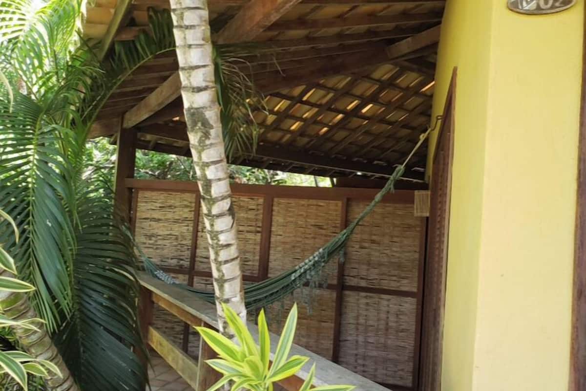 Un hamac suspendu sous une structure de toit en bois, entouré d’une végétation luxuriante.