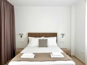Cama bem arrumada com cabeceira marrom, roupa de cama branca e duas luminárias fixadas na parede.