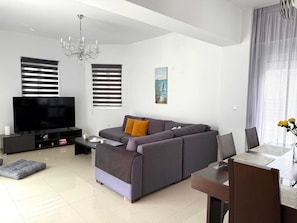 Uma sala de estar moderna com uma televisão de tela plana, um sofá, uma mesa de centro, um candelabro e um quadro na parede.