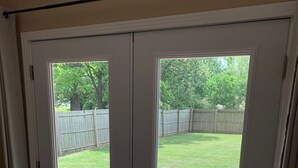 A sliding glass door leading to a backyard with a lawn, a wooden fence, and outdoor furniture.
