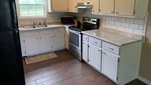 A compact kitchen with white cabinets, a black refrigerator, a microwave, an oven, and a sink.