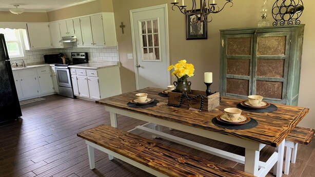 A kitchen with white cabinets, a wooden table with benches, and a chandelier.