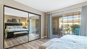 Ein Schlafzimmer mit einem großen Bett, einer Bank, einem Nachttisch, einem Spiegel und einer Glastür, die auf einen Balkon mit Gartenmöbeln führt.