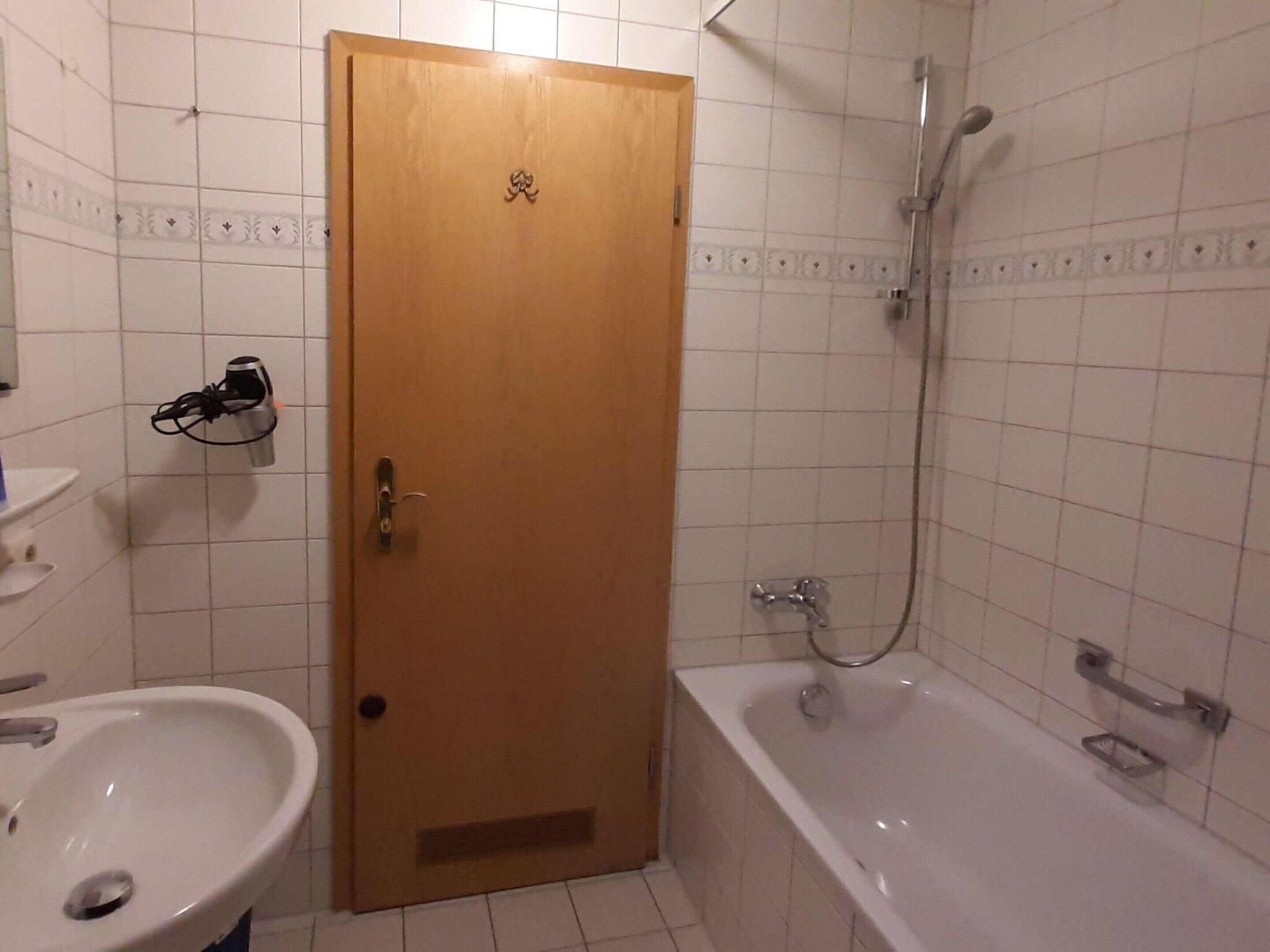 Une salle de bain avec une porte en bois, un lavabo blanc, une baignoire et une douche.