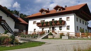A traditional chalet-style building with a steeply pitched roof, a wooden balcony with plants, and a stone staircase leading to the entrance. - Holiday Apartment Tulpe Schuniglhof (Neukirchen Beim Heiligen Blut)
