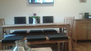 A dining area with a wooden table and chairs, a television mounted on the wall, and a cabinet to the right. - Holiday Apartment Tulpe Schuniglhof (Neukirchen Beim Heiligen Blut)