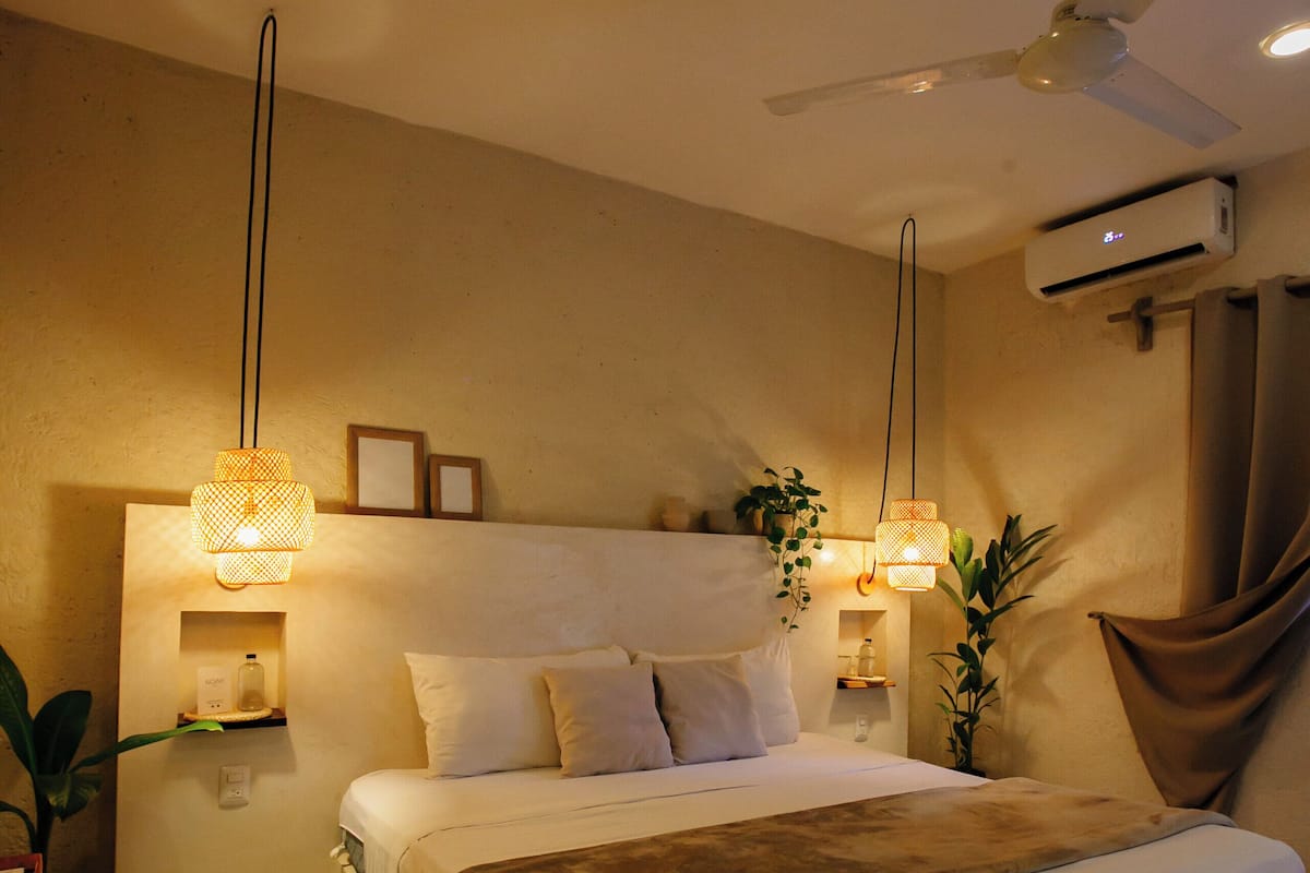 A bedroom with a bed, bedside lamps, a ceiling fan, and a potted plant.