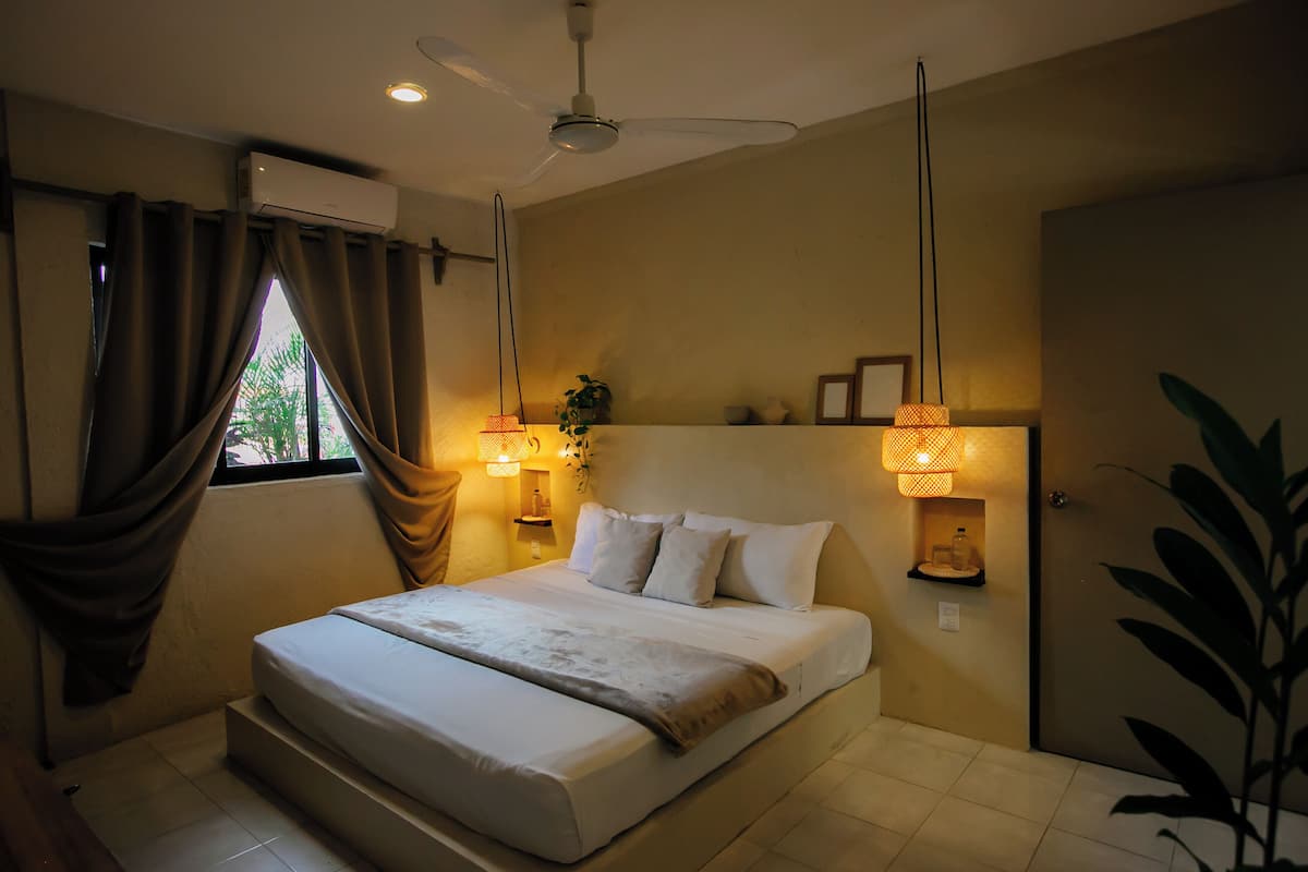 A bedroom with a bed, curtains, a ceiling fan, wall-mounted lamps, and a potted plant.