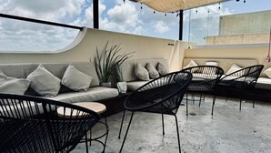 Terraço no telhado com um sofá, duas cadeiras de arame pretas e um vaso com planta.