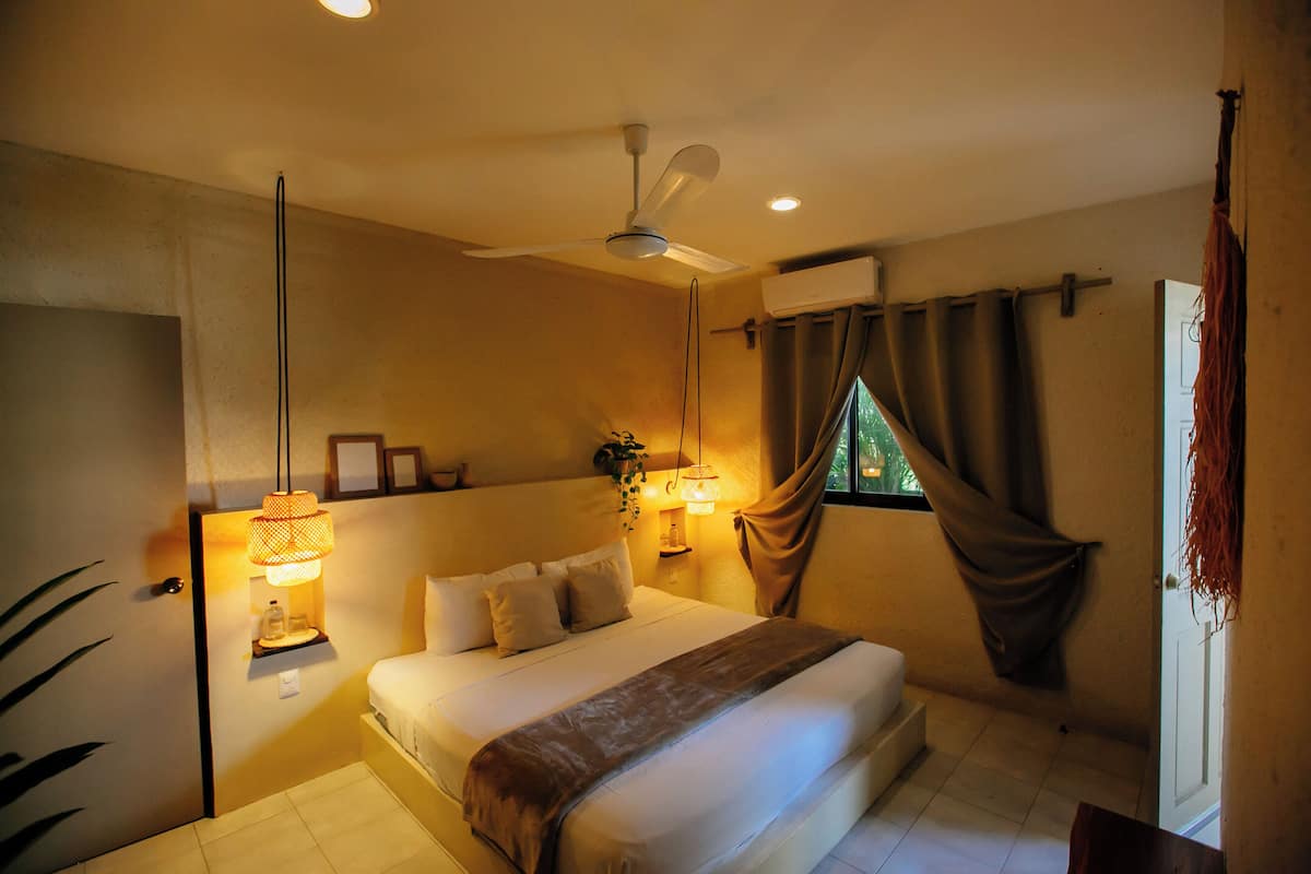 A bedroom with a bed, bedside lamps, a ceiling fan, and a window with curtains.