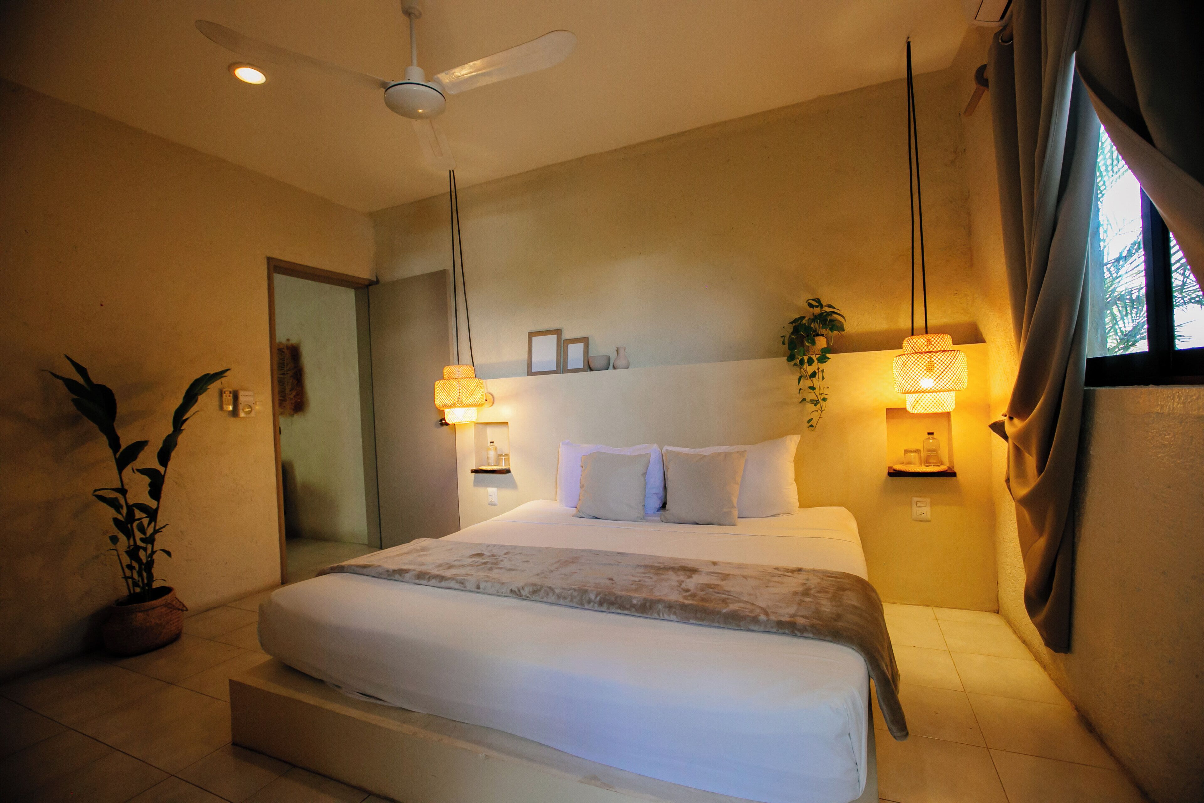 A bedroom with a bed, ceiling fan, bedside lamps, and a potted plant.