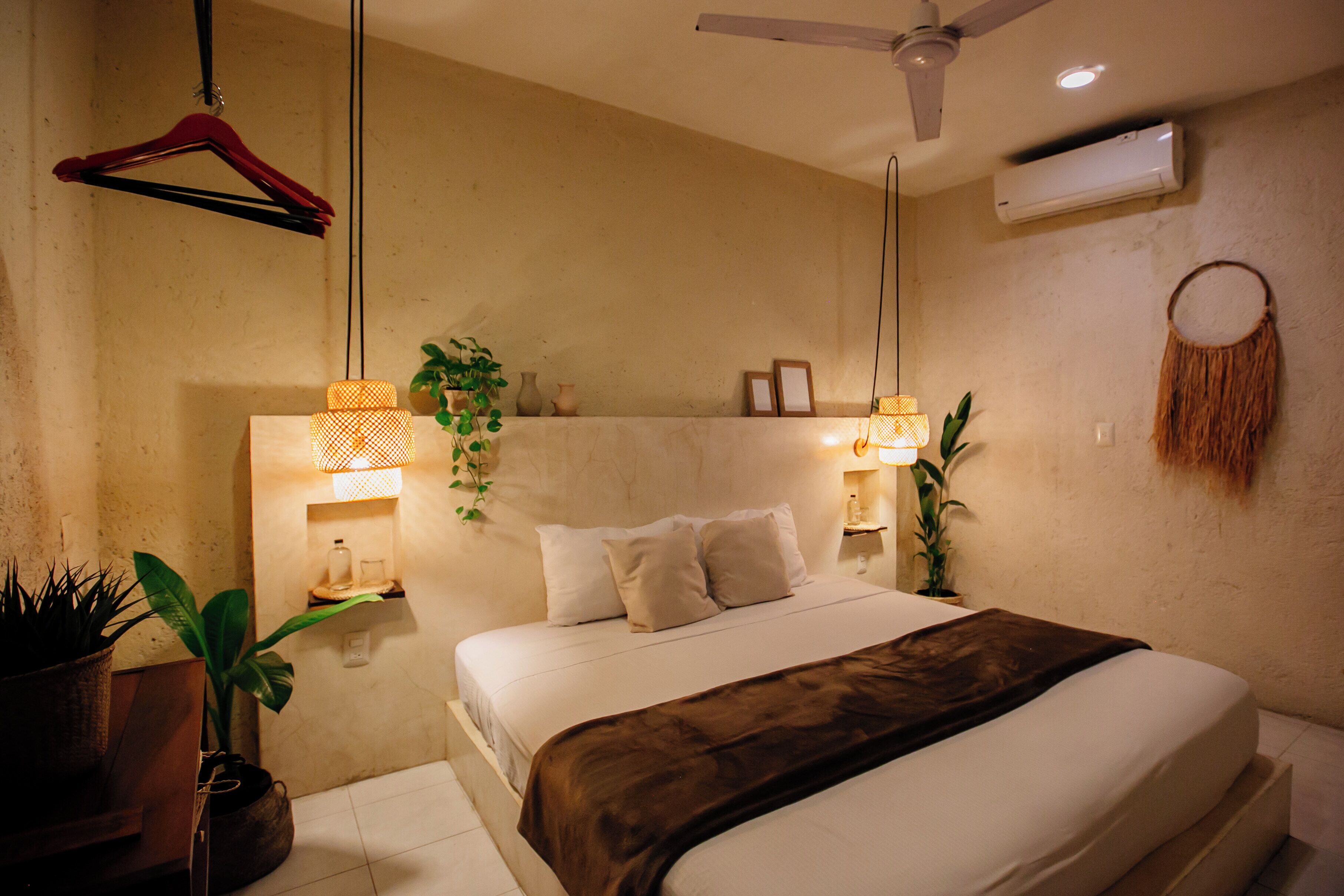 A bedroom with a bed, bedside tables, a ceiling fan, wall-mounted air conditioning, and decorative wall hangings.