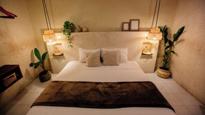 Cama bem arrumada com manta marrom, duas luminárias de cabeceira e duas plantas em vasos.