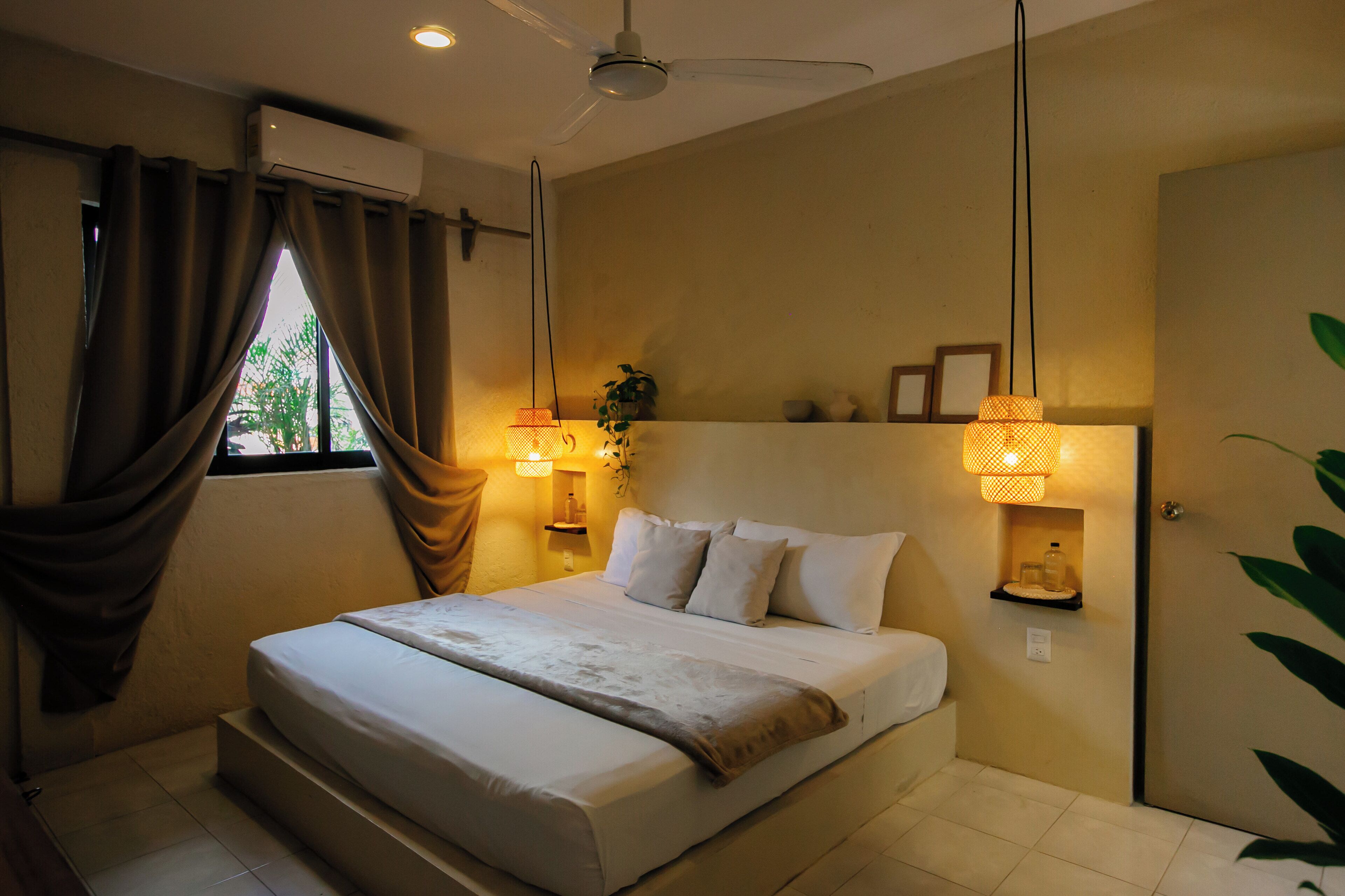 A bedroom with a bed, curtains, a ceiling fan, wall-mounted lamps, and a window.