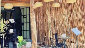 Entrada de um hotel com telhado de palha, área de estar ao ar livre e uma placa indicando 