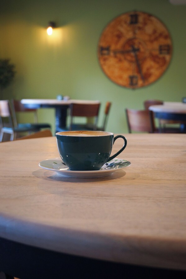 A cup of coffee on a saucer on a table with a clock in the background. - Lemon Tree (Dorchester)