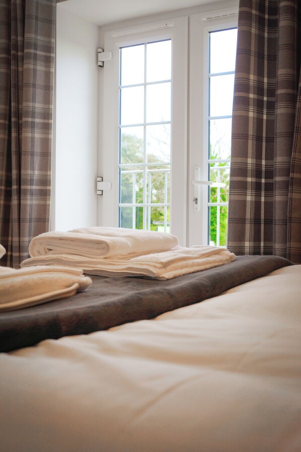 A hotel room with a bed, a window with curtains, and a view of greenery outside. - Lemon Tree (Dorchester)