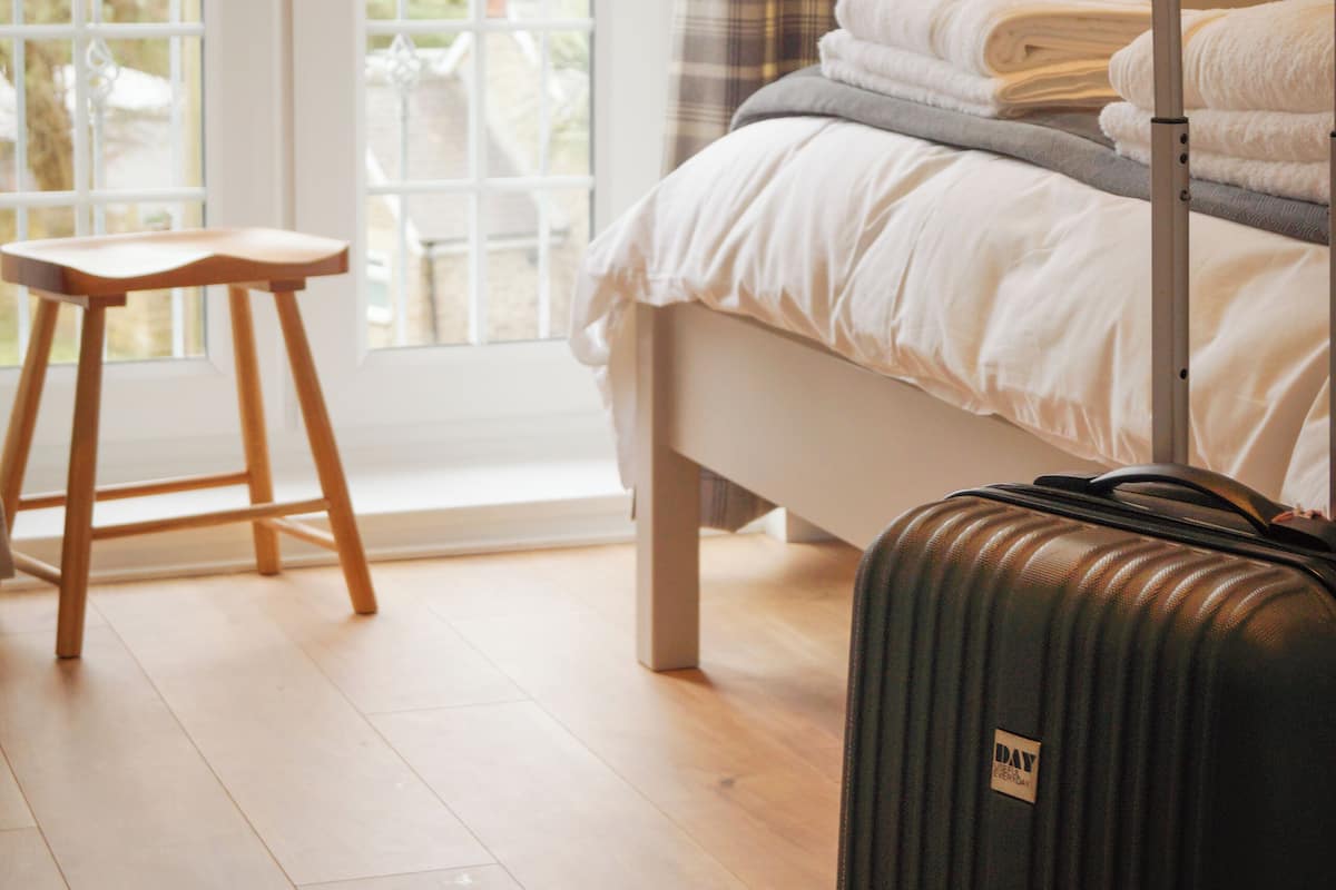A hotel room with a bed, a suitcase, and a wooden stool.