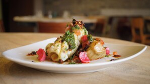 A white plate with a dish of food, including vegetables and possibly meat, on a wooden table. - Lemon Tree (Dorchester)