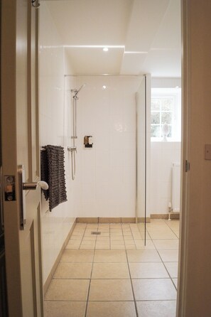 A shower with a glass door, a towel hanging on the wall, and a window with a view of trees. - Lemon Tree (Dorchester)