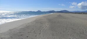 A wide, sandy beach with footprints leading to the water, a clear sky, and distant mountains. - EDO APARTMENT (Sardegna)