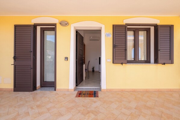 A yellow building with two doors and windows, a doormat, and a sign on the wall. - EDO APARTMENT (Sardegna)