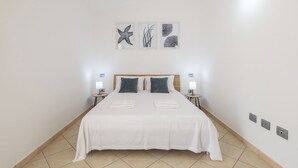 Ein ordentlich bezogenes Bett mit weißer Bettwäsche, zwei Nachttische mit Lampen und drei gerahmte Kunstwerke an der Wand.