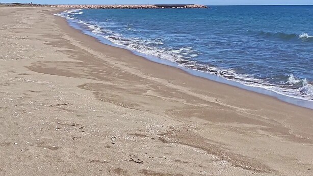 Ein Strand mit einem Felsenmole im Hintergrund.