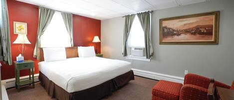 A hotel room with a large bed, two bedside lamps, a painting on the wall, and a red chair.