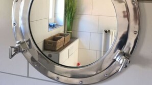 Un miroir rond en métal, doté d’un panneau latéral articulé, fixé sur un mur recouvert de carreaux.