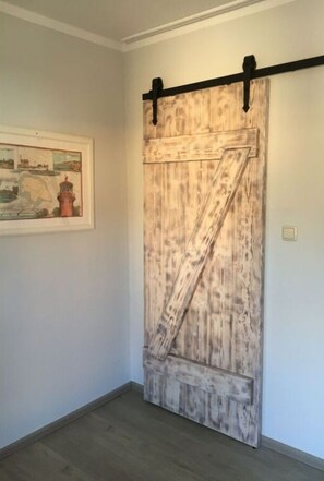 A room with a rustic wooden sliding barn door, a framed landscape painting, and a light switch on the wall. - Sommerhus Fehmarn Comfortable Holiday Residence (Fehmarn)