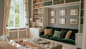 A cozy living room with a green sofa, a beige ottoman, and a bookshelf filled with books. - Agerup Comfortable Holiday Residence (Sakskobing)