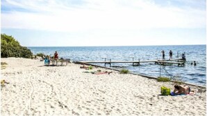 A beach with a wooden pier extending into the water, people walking and relaxing on the sand, and a clear sky. - Agerup Comfortable Holiday Residence (Sakskobing)
