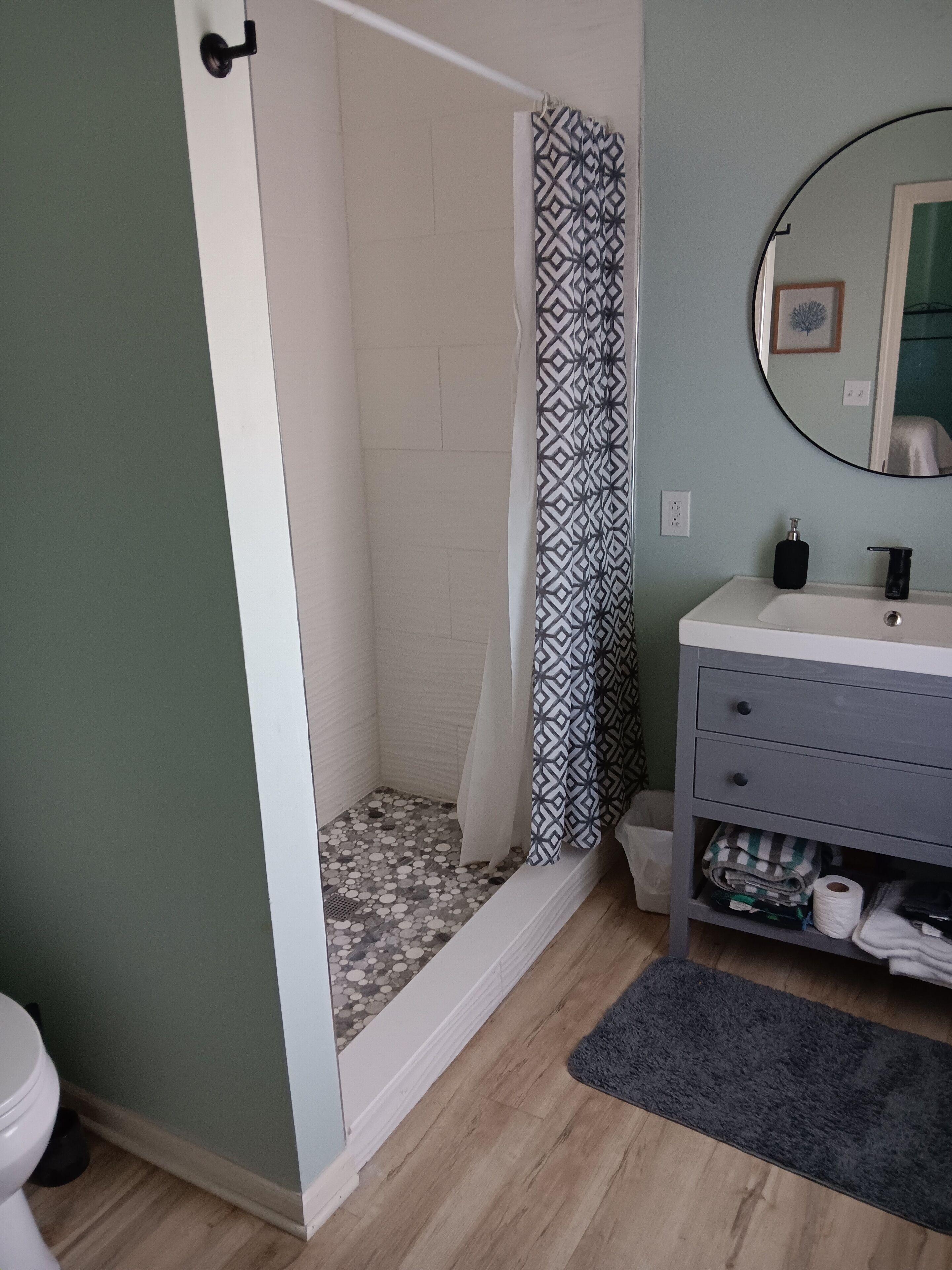 A bathroom with a shower, a sink, a mirror, and a toilet.