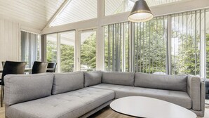 Un salon moderne avec un canapé d’angle gris, une table basse ronde et un coin repas avec des chaises.