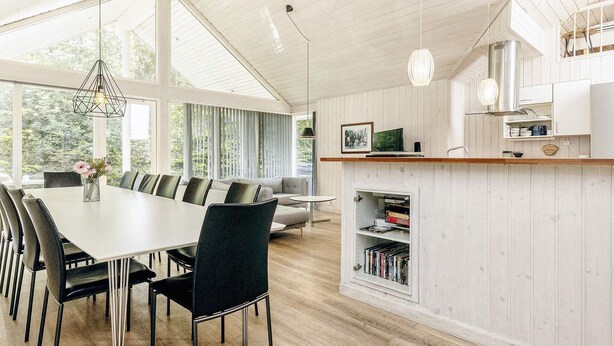 Une cuisine moderne avec des meubles blancs, un coin repas doté d’une grande table et de chaises, et une bibliothèque intégrée.