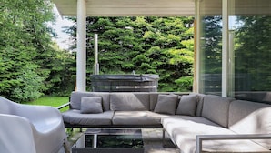 Un espace de vie extérieur moderne comprenant un canapé d’angle, une table basse en verre et une chaise blanche.