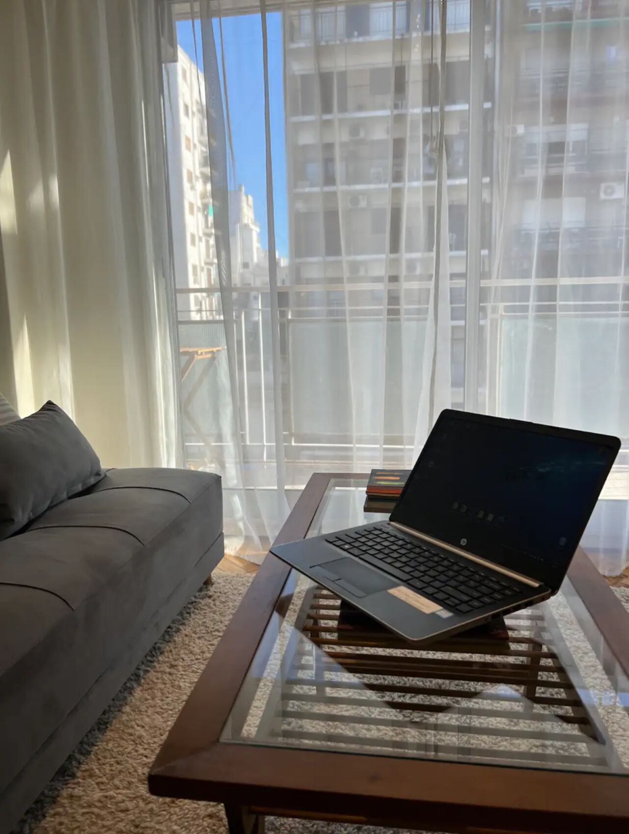 En bærbar computer på et glastop i et rum med en sofa og lette gardiner.