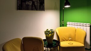 Une pièce avec un mur vert, un tableau abstrait en noir et blanc, un fauteuil jaune, une table ronde avec un plateau en verre et un lampadaire.