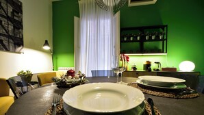 Une table à manger dressée avec des assiettes, des couverts et un verre à vin, avec un mur vert et un rideau blanc en arrière-plan.